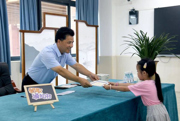 徐龍海用筆在《入學(xué)通知書(shū)》上認(rèn)真寫(xiě)下學(xué)生名字，起身將《入學(xué)通知書(shū)》遞還。金山小學(xué)供圖