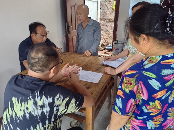 《信手拈來》。7月21日，重慶市二零八地質(zhì)環(huán)境研究院有限公司勘察分院水文地質(zhì)所所長兼潼南區(qū)駐守負(fù)責(zé)人王克峰與潼南區(qū)規(guī)劃和自然資源局梓潼所負(fù)責(zé)人米澤坤，在梓潼街道社區(qū)一戶農(nóng)戶家里給戶主介紹如何做好房前屋后邊坡防治，王克峰隨手用筆在手上畫出邊坡輪廓。李鋒俊攝