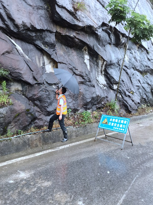 《看·守》。6月23日，208地質(zhì)隊駐守隊員曹銳在北碚區(qū)天府鎮(zhèn)雨中巡查公路邊坡。