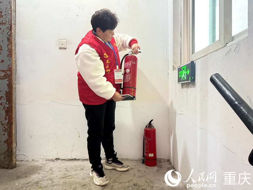 文登群認(rèn)真檢查樓梯間擺放的滅火器是否能正常使用。人民網(wǎng)記者 胡虹攝